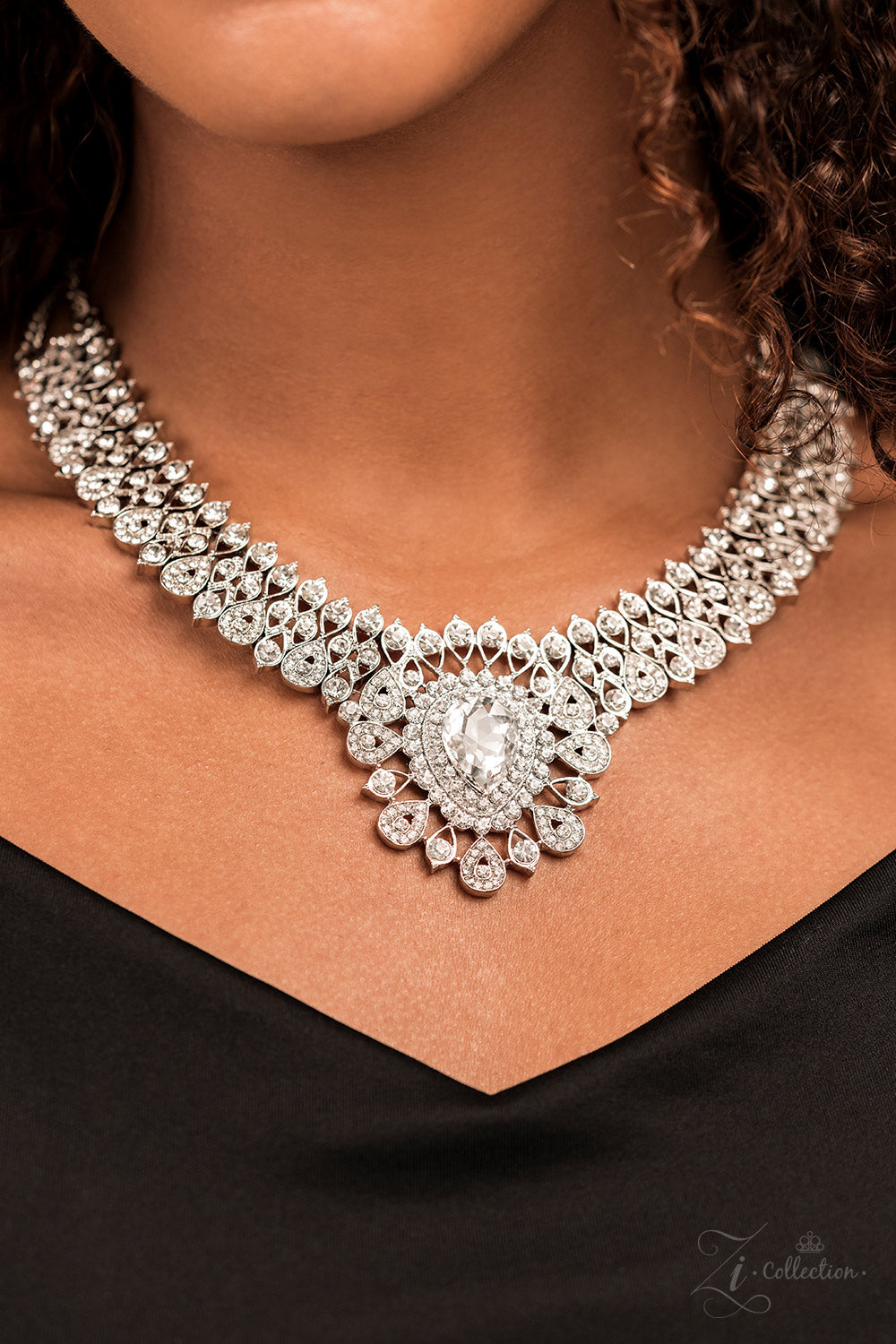 Silver, teardrop-shaped frames are stacked on-point below airy marquise cutouts, creating a subtle figure-eight. The hourglass shapes are threaded along invisible wires, falling into place alongside diamond-shaped frames, created by artfully aligned, smaller, teardrop silhouettes. Glittery rhinestones encrust the larger teardrop-shaped frames, with solitaire rhinestones dotting the others; the result is a blinding display of irresistible shimmer that leads to a heart-stopping centerpiece.