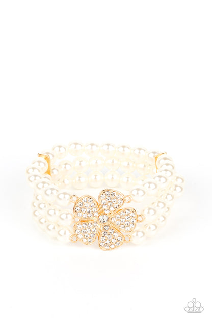 Park Avenue Orchard Gold Pearl Bracelet - Paparazzi Accessories  Separated by dainty gold plates, classic white pearls are threaded along three stretchy bands around the wrist. Encrusted in glassy white rhinestones, a glitzy gold flower blooms at the center of the wrist for a fierce floral statement.  Sold as one individual bracelet.