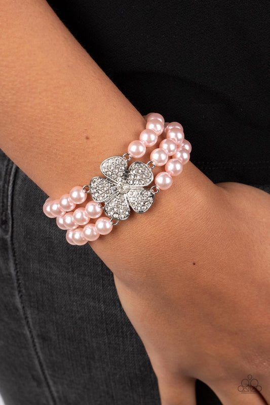 Park Avenue Orchard Pink Bracelet - Paparazzi Accessories  Separated by dainty silver plates, bubbly pink pearls are threaded along three stretchy bands around the wrist. Encrusted in glassy white rhinestones, a glitzy silver flower blooms at the center of the wrist for a fierce floral statement.  Sold as one individual bracelet.