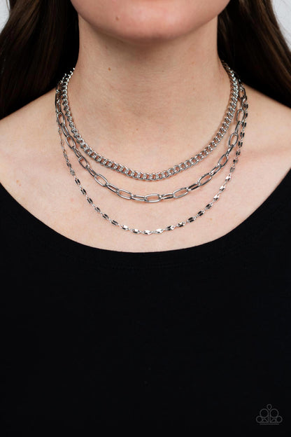 Galvanized Grit Silver Necklace - Paparazzi Accessories  Three different kinds of weighted silver chains layer down the neck to create a gritty, edgy statement piece. Features an adjustable clasp.  Sold as one individual necklace. Includes one pair of matching earrings.
