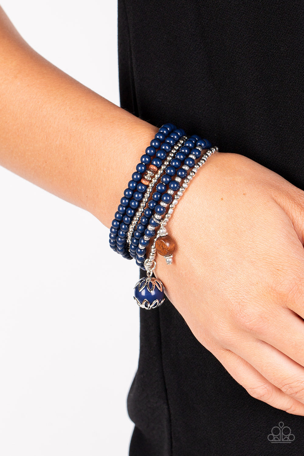 Epic Escapade Blue Bracelet - Paparazzi Accessories  A mismatched collection of silver, navy blue, and wooden beads are threaded along stretchy bands around the wrist. An ornate navy blue and wooden bead trickles from the layers, adding whimsical accents to the earthy display.  Sold as one set of six bracelets.  P9SE-BLXX-416XX