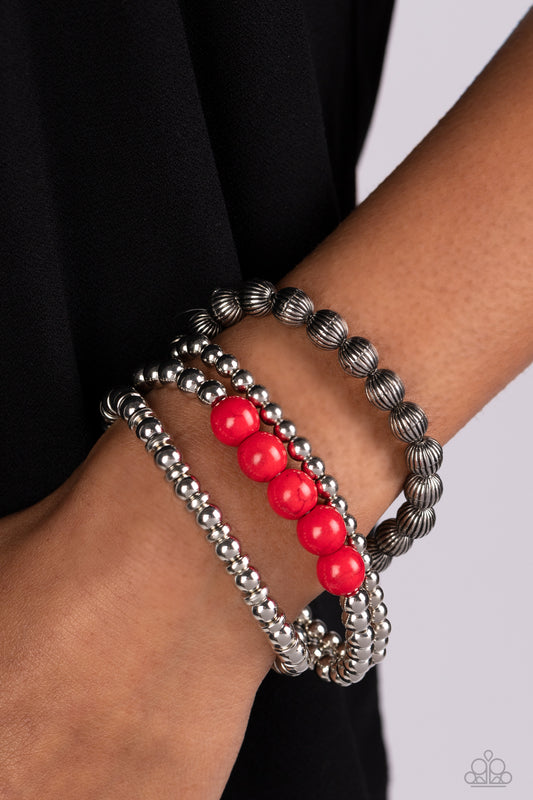 Wildland Wanderer Red Bracelet - Paparazzi Accessories  Strands of small silver beads polished in a high sheen finish stack together with a strand of silver beads etched in linear patterns. A row of fiery red stones pops against the backdrop of metallic shimmer, as the stretchy bands are bundled together by a pair of silver rings. As the stone elements in this piece are natural, some color variation is normal.  Sold as one set of four bracelets.