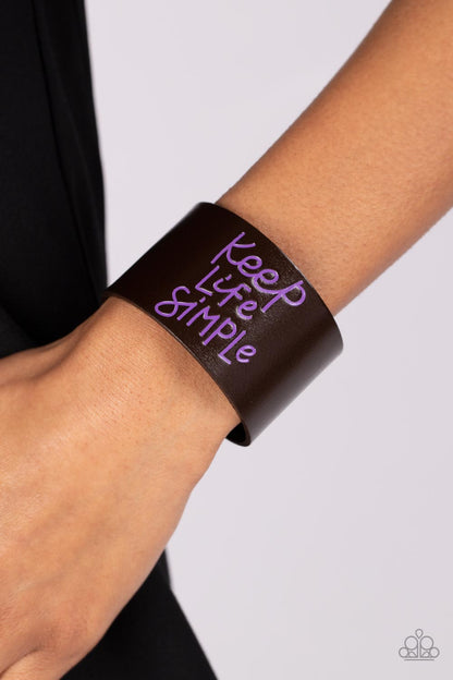 Simply Stunning Purple Wrap Bracelet - Paparazzi Accessories  A thick band of dark brown leather is stamped in the phrase, "Keep Life Simple," in purple script. The playful font emphasizes the lighthearted message as the band wraps around the wrist in a casual finish. Features an adjustable snap closure.  Sold as one individual bracelet.