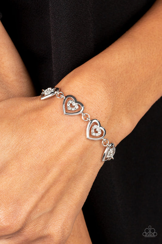Catching Feelings White Bracelet - Paparazzi Accessories  Dotted with dainty white rhinestones, airy silver heart silhouettes are affixed to the points of larger silver heart frames. The two dimensional heart frames link together around the wrist in a flirtatious finish. Features an adjustable clasp closure.  Sold as one individual bracelet.