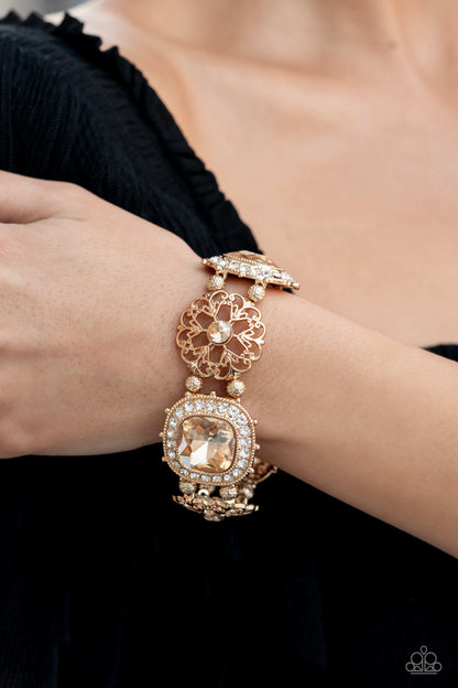 Gilded Gallery Gold Bracelet - Paparazzi Accessories   Oversized faceted golden gems in dramatically rounded square cuts are wrapped in borders of classic white rhinestones, emitting a breathtaking sheen. Floral-inspired frames, dotted with solitaire golden rhinestones, bloom in between the large rhinestones, adding airy accents to the bold design, as textured gold beads separate each frame as they're threaded along stretchy elastic bands.  Sold as one individual bracelet.  December 2022 Life of the Party!