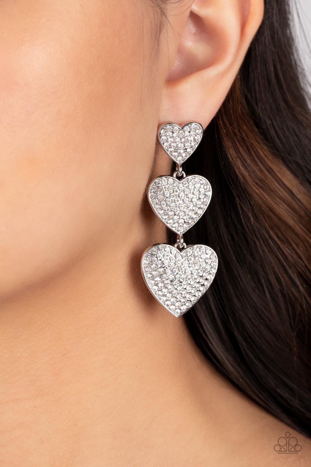 Couples Retreat White Heart Post Earring - Paparazzi Accessories  Three white rhinestone-studded silver hearts gradually increase in size as they cascade down the ear in a shimmery display. Each of the hearts interconnect to one another adding a shifting, whimsical detail to the spritz of glitz. Earring attaches to a standard post fitting.  Sold as one pair of post earrings.