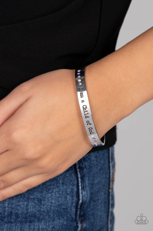 Divine Display Multi Cuff Bracelet - Paparazzi Accessories  A shiny silver cuff stamped with the phrase "I am a Child of God" encircles the wrist. Dainty sapphire, violet and iridescent rhinestones shimmer at the borders of the phrase for a whimsical finish. Due to its prismatic palette, color may vary.  Sold as one individual bracelet.