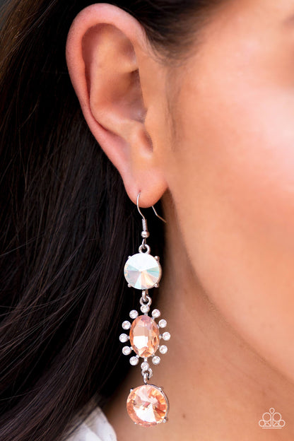 A trio of colorfully iridescent and brilliantly sparkling peach gems are linked together as they fall glamorously from the ear. A round-cut gem with an exaggerated faceted surface anchors the cascade, followed by an oval-cut peach rhinestone bordered in classic white rhinestones. Another round-cut gem — this one in a peach hue — finishes off the design in a sparkling finish. Earring attaches to a standard fishhook fitting. Due to its prismatic palette, color may vary.  Sold as one pair of earrings.