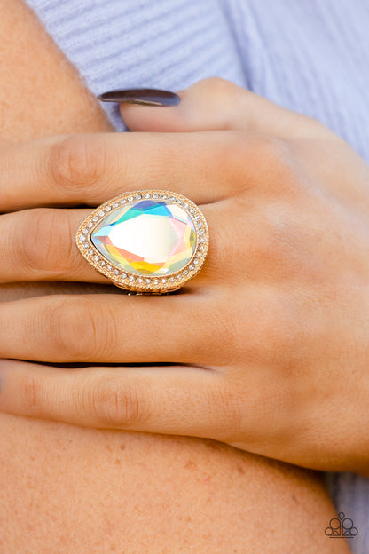 Illuminated Icon Gold Ring - Paparazzi Accessories  An oversized teardrop gem with an iridescent finish is nestled inside a gold teardrop frame encrusted in dainty white rhinestones. Airy teardrop cutouts decorate each side of the oversized frame### some with subtle texture and others with a high sheen finish. Features a stretchy band for a flexible fit. Due to its prismatic palette### color may vary.  Sold as one individual ring.