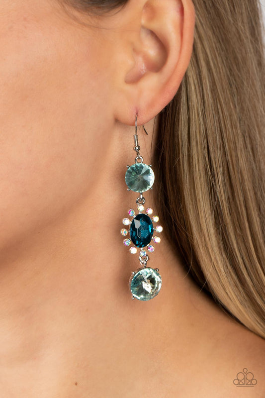 Magical Melodrama Blue Earring - Paparazzi Accessories  A trio of colorfully iridescent and brilliantly sparkling blue gems are linked together as they fall glamorously from the ear. A round-cut gem with an exaggerated faceted surface anchors the cascade, followed by an oval-cut navy rhinestone bordered in iridescent rhinestones. Another round-cut gem finishes off the design in a sparkling finish. Earring attaches to a standard fishhook fitting. Due to its prismatic palette, color may vary.
