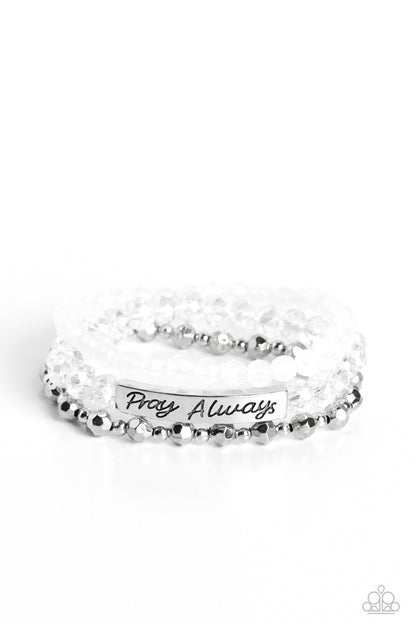 Pray Always White Bracelet - Paparazzi Accessories  Varying in shape and shimmer, faceted silver beads, milky white beads, and glittery crystal-like beads are threaded along elastic stretchy bands, creating colorful layers across the wrist. Featured on the crystal-like band, a curved silver bar features the words "Pray Always" in a curly, stamped font for a soft finish.  Sold as one individual bracelet.