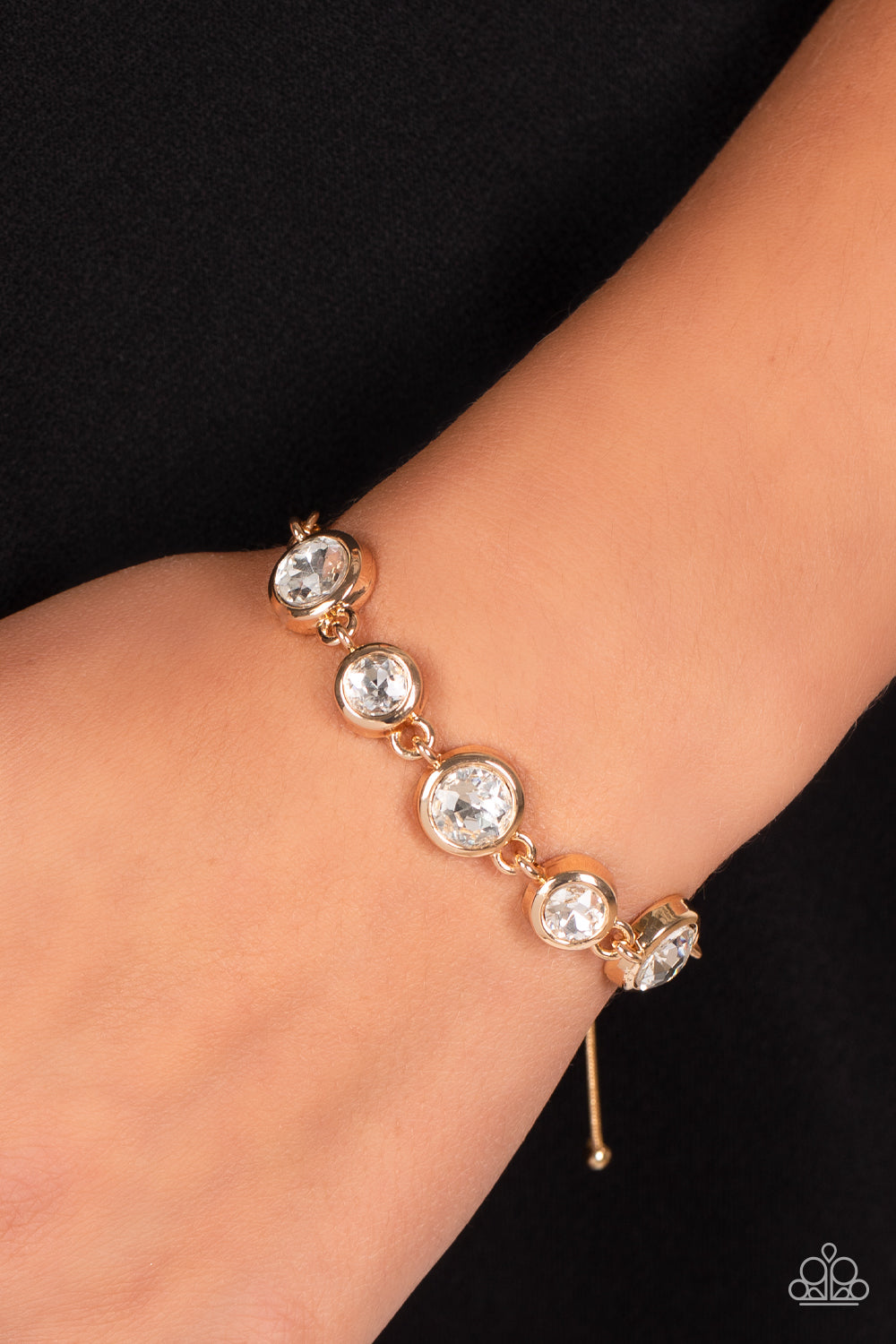 Classically Cultivated Gold Bracelet - Paparazzi Accessories  Varying sizes of classic, round, brilliant-cut white rhinestones set in thick, circular, gold frames link together around the wrist with glamorous glimmer. The rhinestones attach to a dainty strand of gold snake chain that wraps around the wrist in a refined finish. Features an adjustable lariat sliding bead closure.  Sold as one individual bracelet.
