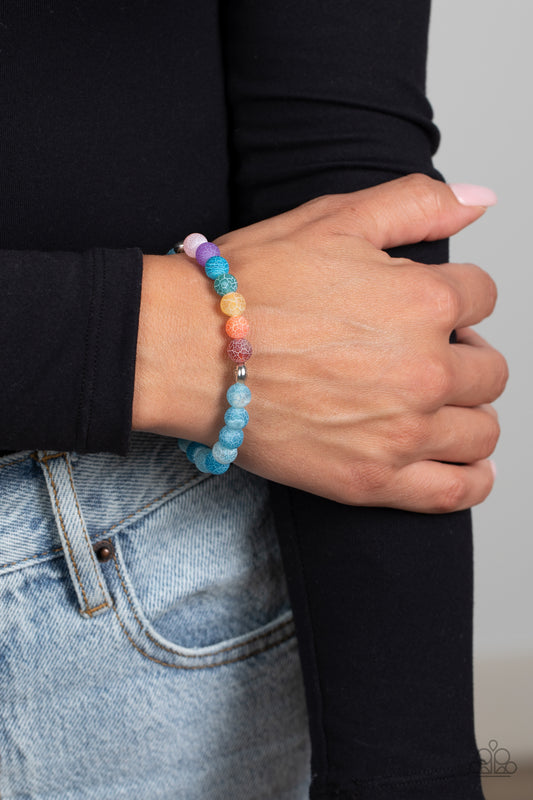 Lotus Chakra Blue Unisex Stretch Bracelet - Paparazzi Accessories  A collection of refreshing blue stone beads with speckled detailing, and stone beads brushed in the shades of the rainbow are threaded along a stretchy band around the wrist for a seasonal finish. Separating the chakra-inspired stones from the refreshing blue stones, two silver beads, stamped with a lotus flower outline add a floral feature to the urban design. 