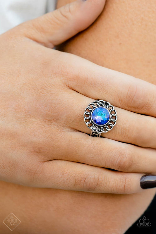 Round Table Runway Blue Ring - Paparazzi Accessories  High-sheen silver chain links encircle a vibrant, faceted blue gem center, creating a gorgeous contrast of grit and glam. A band of silver chain link arcs across the finger underneath the colorful centerpiece, resulting in an edgy centerpiece that sits boldly atop the finger. Features a dainty stretchy band for a flexible fit.  Sold as one individual ring.