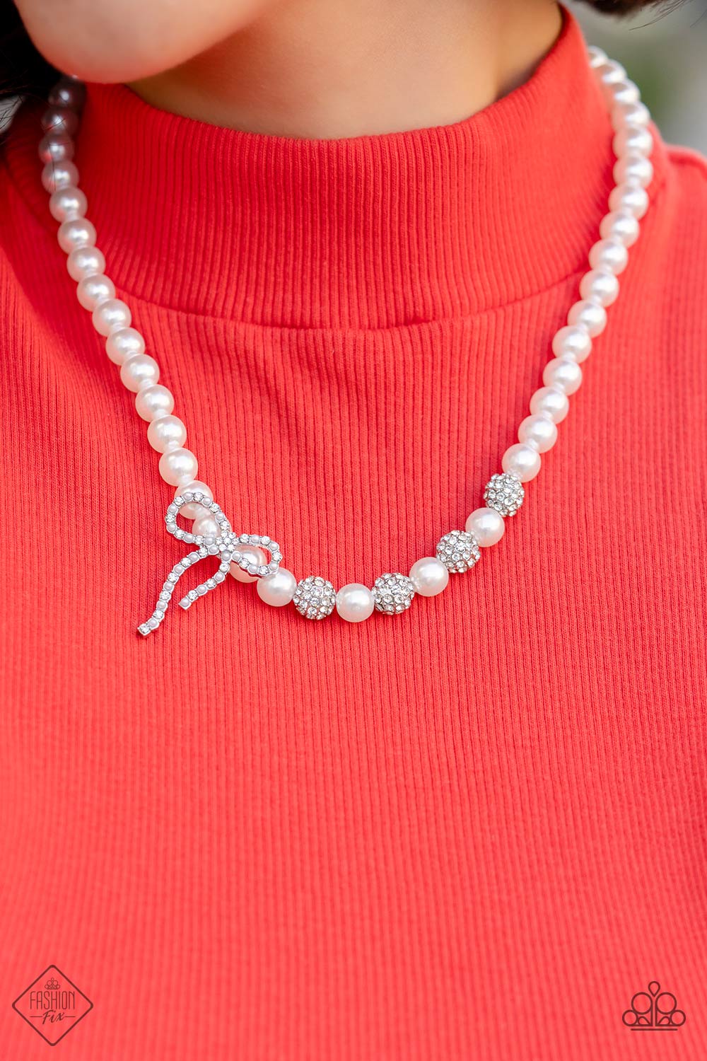 Classy Cadenza White Pearl Necklace - Paparazzi Accessories  A strand of classic white pearls coalesces down the neckline in a feminine display. Airy silver spheres, adorned in sparkling white rhinestones, are effortlessly sprinkled among the sea of pearls on one side, infusing the design with capricious shimmer. Then in the perfect finishing touch, a ribbon of silver, adorned in tiny white pearls and sparkling white rhinestones, loops into a bow at the bottom of the design.