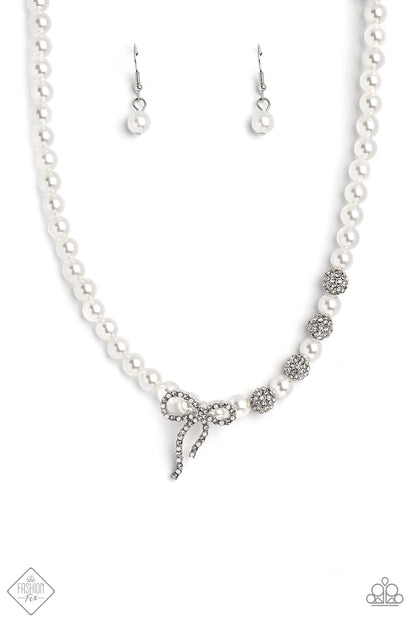 Classy Cadenza White Pearl Necklace - Paparazzi Accessories  A strand of classic white pearls coalesces down the neckline in a feminine display. Airy silver spheres, adorned in sparkling white rhinestones, are effortlessly sprinkled among the sea of pearls on one side, infusing the design with capricious shimmer. Then in the perfect finishing touch, a ribbon of silver, adorned in tiny white pearls and sparkling white rhinestones, loops into a bow at the bottom of the design.