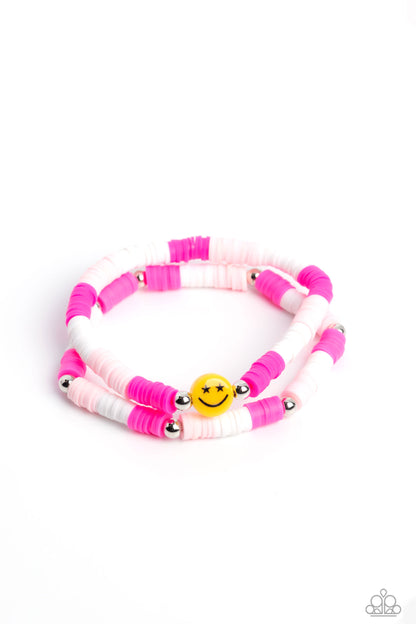 In SMILE Pink Bracelet - Paparazzi Accessories  Hot pink, baby pink, and white rubber discs combine with sporadically placed silver beads to provide a vibrant pop of color along the wrist. Meeting in the center of one of the pink-shaded bracelets, a yellow bead with a smiley face, featuring stars for eyes, rests for a youthful finish.  Sold as one set of two bracelets.  P9SE-PKXX-172XX