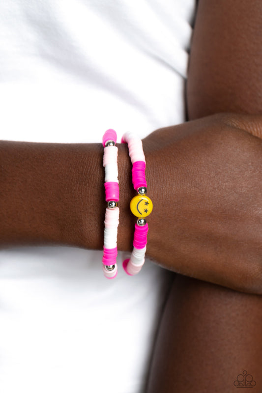 In SMILE Pink Bracelet - Paparazzi Accessories  Hot pink, baby pink, and white rubber discs combine with sporadically placed silver beads to provide a vibrant pop of color along the wrist. Meeting in the center of one of the pink-shaded bracelets, a yellow bead with a smiley face, featuring stars for eyes, rests for a youthful finish.  Sold as one set of two bracelets.  P9SE-PKXX-172XX