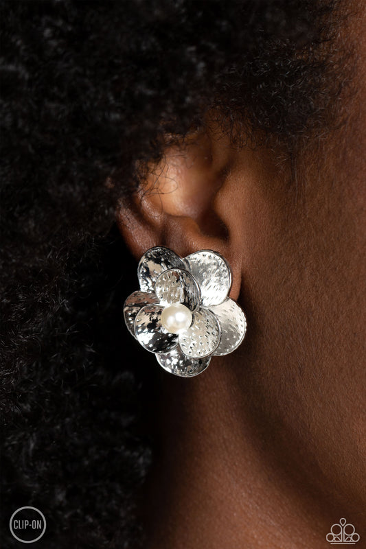 Miami Magic White Clip-On Earring - Paparazzi Accessories  Flaring out from a white pearl center, silver flowers, featuring studded petals, grace the ear. An oversized silver flower, featuring the same studded design as the smaller flower, creates the 3D design and draws additional attention to the whimsical design. Earring attaches to a standard clip-on fitting.  Sold as one pair of clip-on earrings.  P5CO-WTXX-141XX