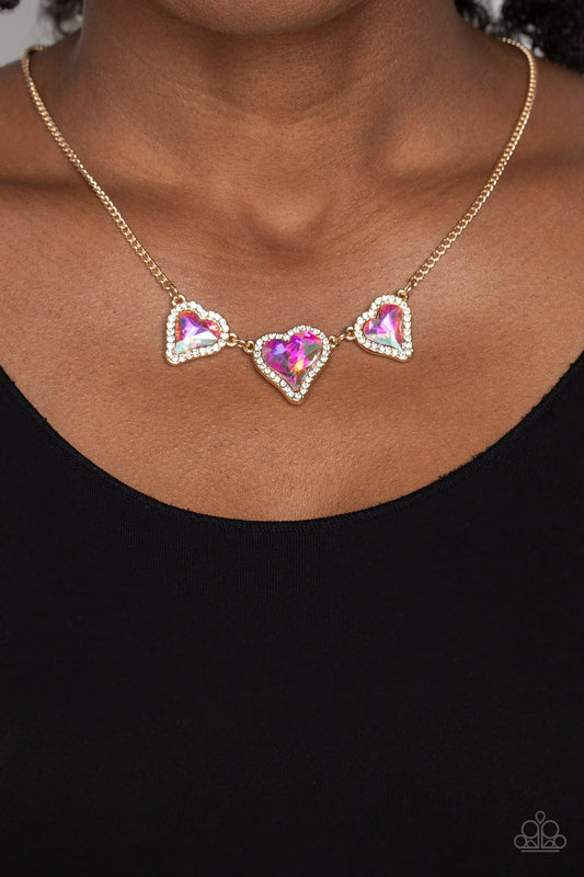 State of the HEART Gold Necklace - Paparazzi Accessories  Nestled in white rhinestone frames, a trio of glittery iridescent heart-shaped gems delicately links and dangles down the neckline for a dash of swoon-worthy shimmer on a gold chain. Features an adjustable clasp closure. Due to its prismatic palette, color may vary.  Sold as one individual necklace. Includes one pair of matching earrings.  P2RE-GDXX-456XX