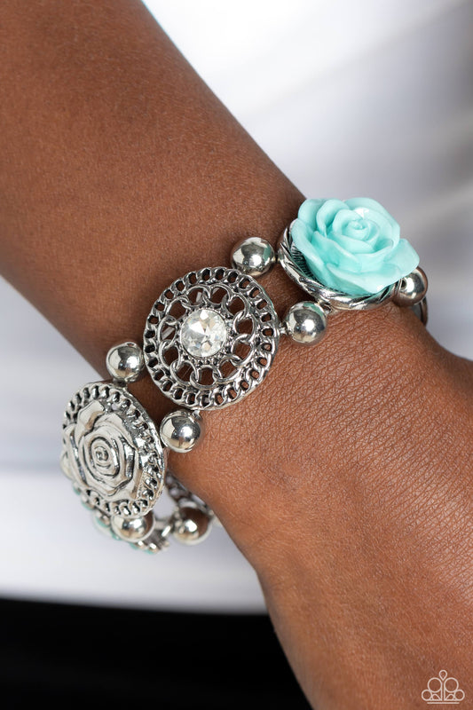 Optimistic Oasis Blue Bracelet - Paparazzi Accessories  Whimsically woven around the wrist on elastic stretchy bands, a Spun Sugar resin rose, a silver disc stamped with a paisley motif, an oversized white gem encased in a textured silver frame, an airy, textured wheel pendant with a white center, a pearl-centered flower with Spun Sugar gem petals, and a disc featuring a metallic rose, create a beautifully botanical design. Classic silver beads separate each element.  P9ST-BLXX-030XX