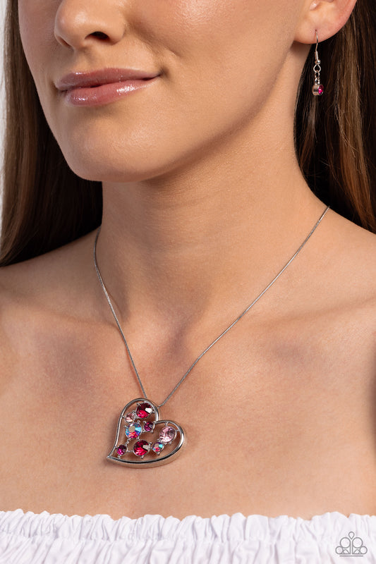Romantic Recognition Pink Rhinestone Heart Necklace - Paparazzi Accessories  Cascading from a silver snake chain, a thick, sideways sliding-heart silhouette falls down the neckline for a romantic statement. Haphazardly scattered across the inside of the heart frame, a glittery collection of pink and iridescent fuchsia round rhinestones in varying sizes shimmer and shine for a refined finish. Features an adjustable clasp closure. Due to its prismatic palette, color may vary.