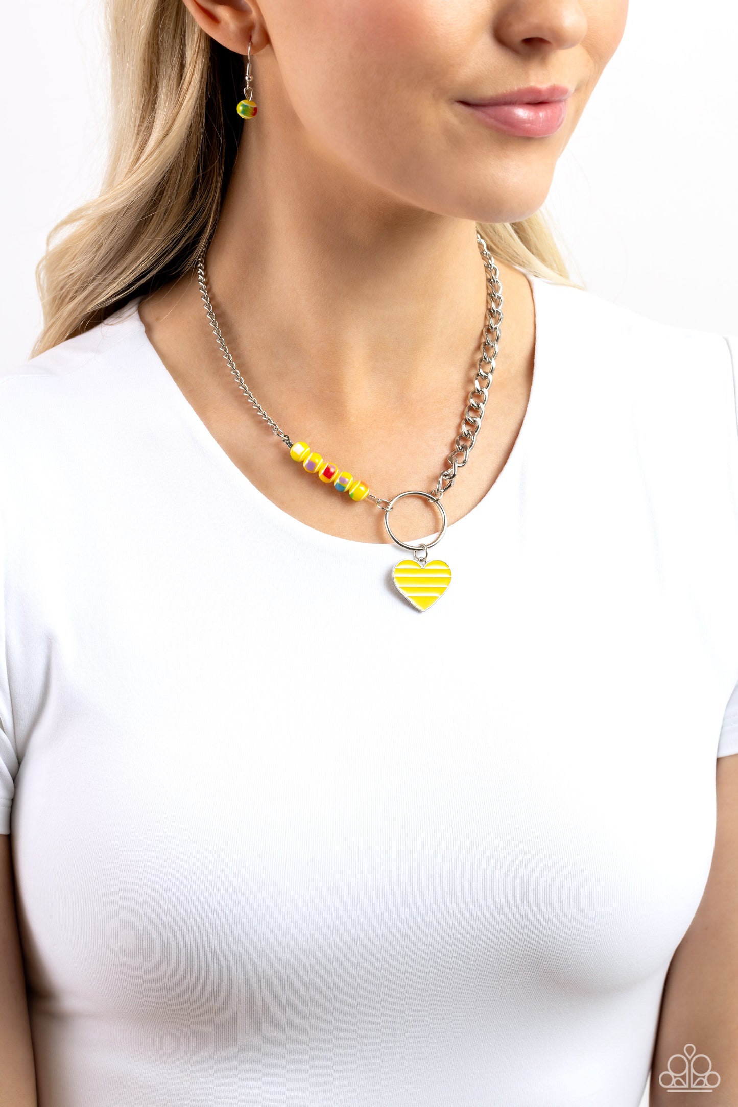 Mismatched Mayhem Yellow Heart Necklace - Paparazzi Accessories  A strand of flat silver curb chain collides with a classic chain and a vivacious collection of yellow beads, featuring various multicolored splatters across its surface, to create an abstract blend of color and class. The mismatched chains connect to a large silver hoop with a yellow-striped silver heart dangling at the bottom of the display, infusing the design with additional charm. Features an adjustable clasp closure.