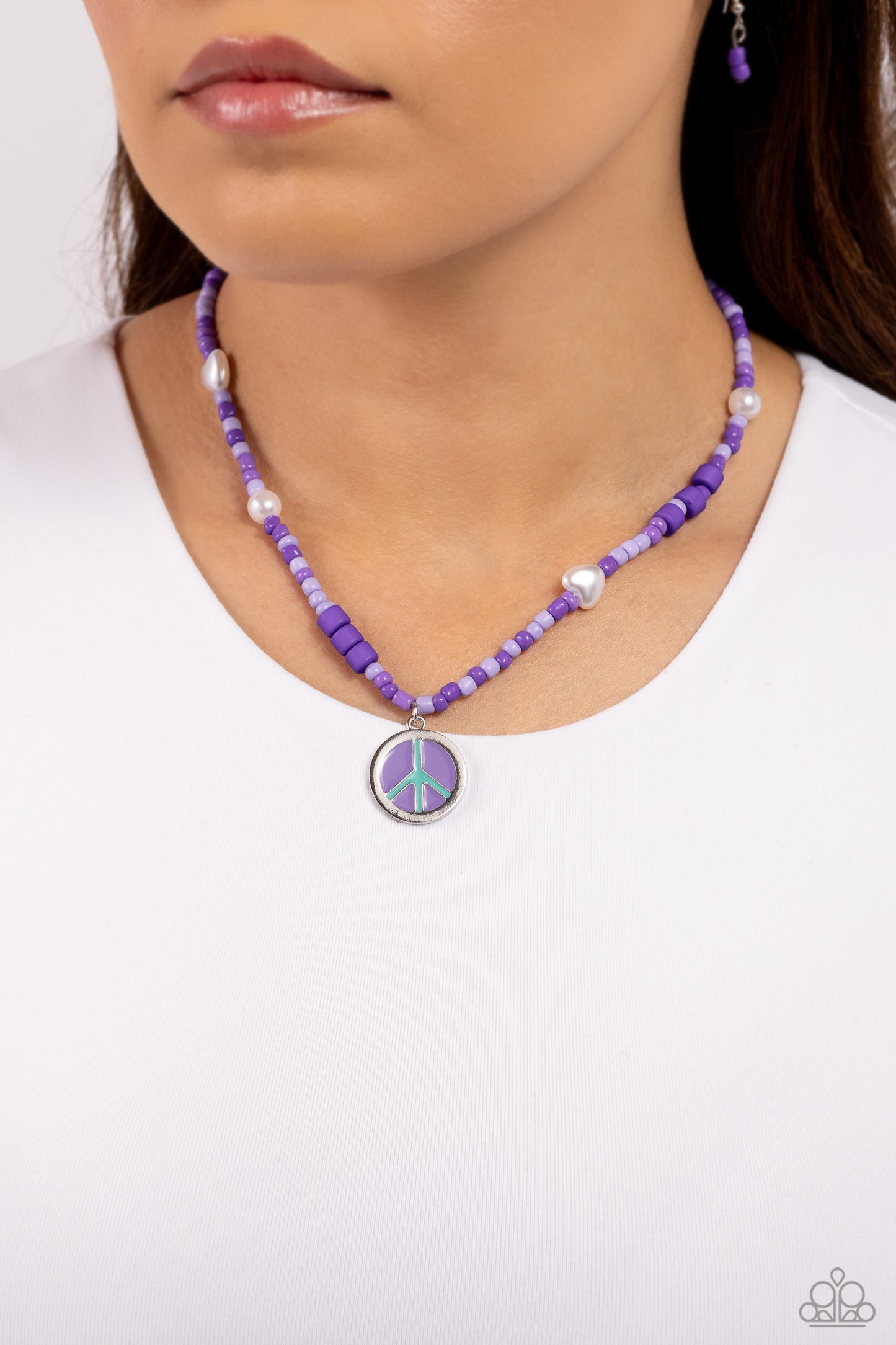 Pearly Possession Purple Necklace - Paparazzi Accessories  Infused along an invisible string, lavender, plum, and purple seed beads combine with sporadically placed purple discs, and glossy white and heart-shaped pearls for a vibrant pop of color along the neckline. A silver peace sign featuring blue and purple paint dangles from the colorful strand for a groovy finish. Features an adjustable clasp closure.  Sold as one individual necklace. Includes one pair of matching earrings.  P2DA-PRXX-141XX