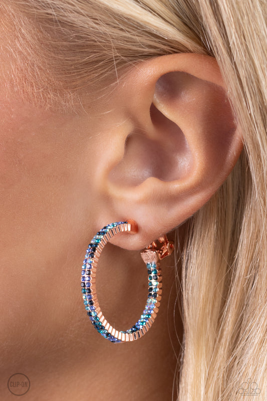 Outstanding Ombre Copper Clip-On Earring - Paparazzi Accessories  The front half and lower inner curve of a textured shiny copper hoop are encrusted in dazzling ombré shades of blue for a flawless look. Earring attaches to a standard clip-on fitting. Hoop measures approximately 1" in diameter. Due to its prismatic palette, color may vary.  Featured inside The Preview at Made for More!  Sold as one pair of clip-on earrings.  P5CO-CPSH-032XX