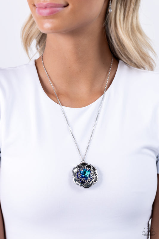 Pressed in the center of an oversized, thick silver floral frame, a blue UV gem glimmers from the chest. Intricate silver hearts, sprinkled with dainty white rhinestones, encircles the inner circle of the floral frame to create ornate, 3D petals. The whimsical pendant swings from the bottom of a lengthened, dainty silver chain for a seasonal look. Features an adjustable clasp closure.  Sold as one individual necklace. Includes one pair of matching earrings.  P2RE-BLXX-414XX
