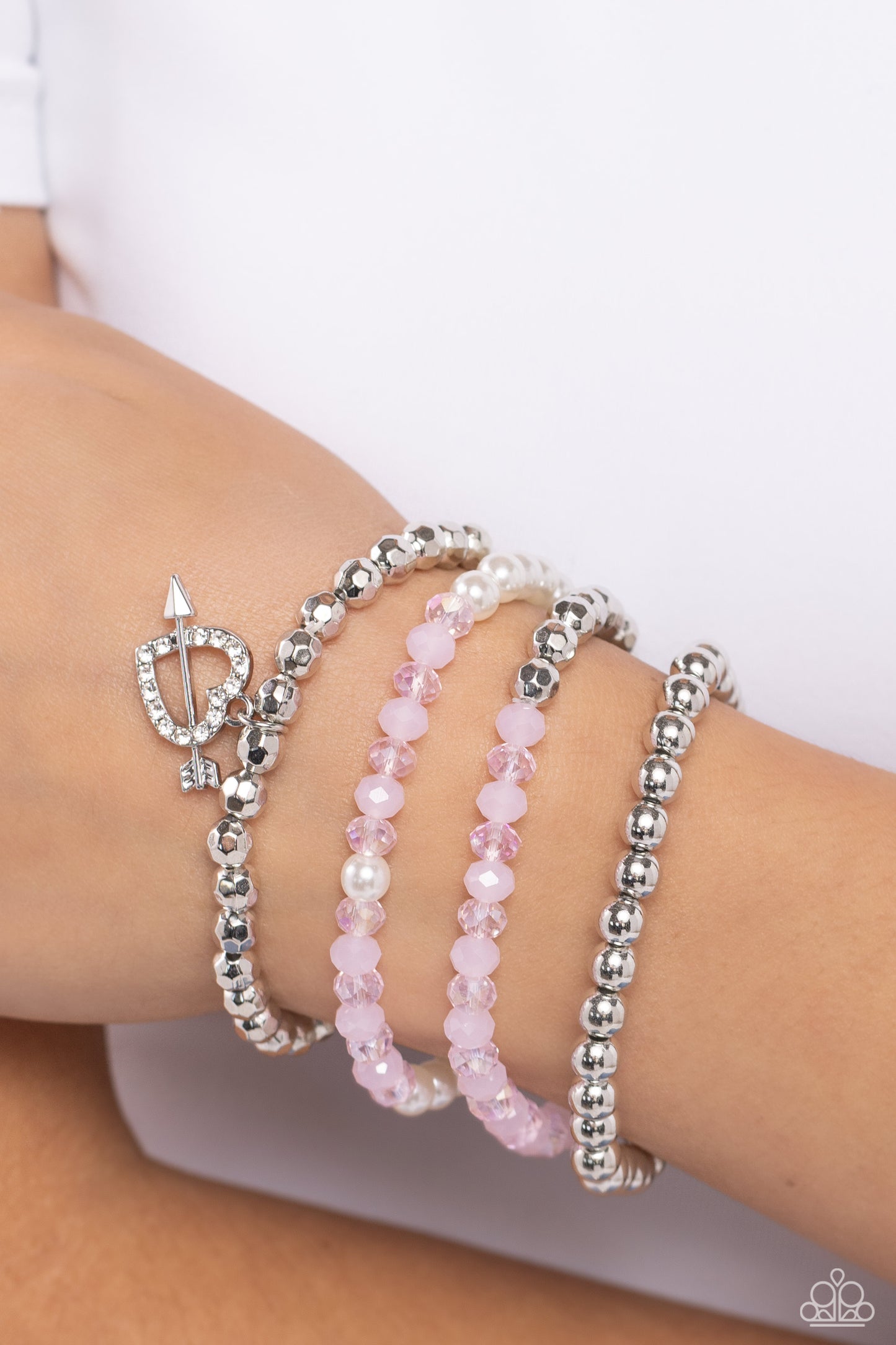 Heart-struck Haute Pink Stretch Bracelet - Paparazzi Accessories  A mismatched collection of faceted silver beads, sleek silver beads, bubbly white pearls, crystal-like pink beads, and opaque pink beads are threaded along stretchy bands around the wrist, creating vivacious layers. An airy rhinestone-encrusted heart charm with a silver arrow dangles from one of the strands for additional romantic flair.  Sold as one set of four bracelets.  SKU: P9RE-PKXX-319XX