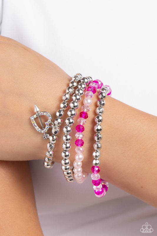 Heart-struck Haute Multi Stretch Bracelet - Paparazzi Accessories  A mismatched collection of faceted silver beads, sleek silver beads, bubbly pink pearls, and crystal-like pink and fuchsia beads are threaded along stretchy bands around the wrist, creating vivacious layers. An airy iridescent rhinestone-encrusted heart charm with a silver arrow dangles from one of the strands for additional romantic flair. Due to its prismatic palette, color may vary.