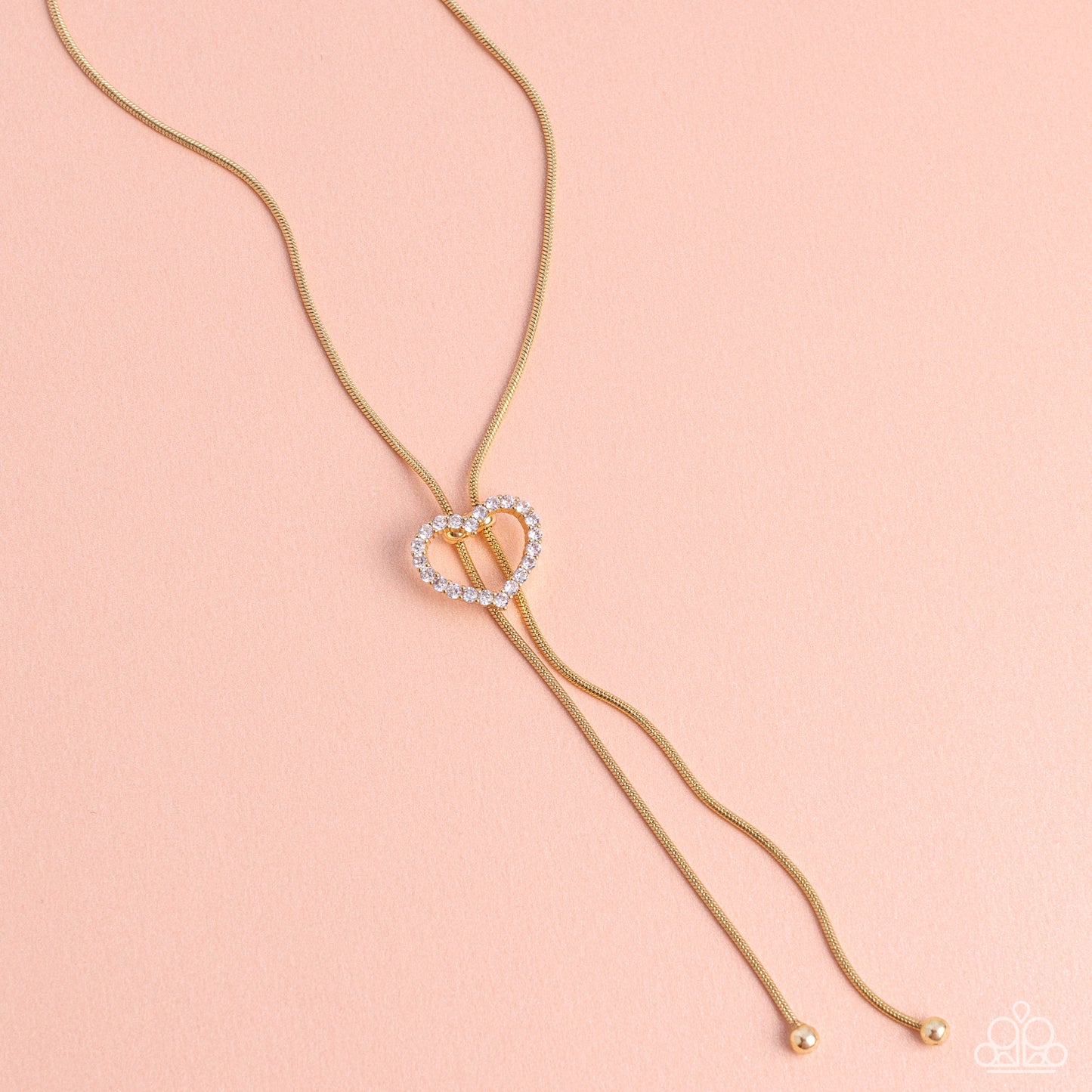 Tempting Tassel Gold Heart Bolo Necklace - Paparazzi Accessories  A dainty white rhinestone-encrusted heart silhouette slides along dainty strands of glistening gold snake chain for a timeless, refined tassel. Features a bolo closure.  Sold as one individual necklace. Includes one pair of matching earrings.  Sku:  P2DA-GDXX-327XX