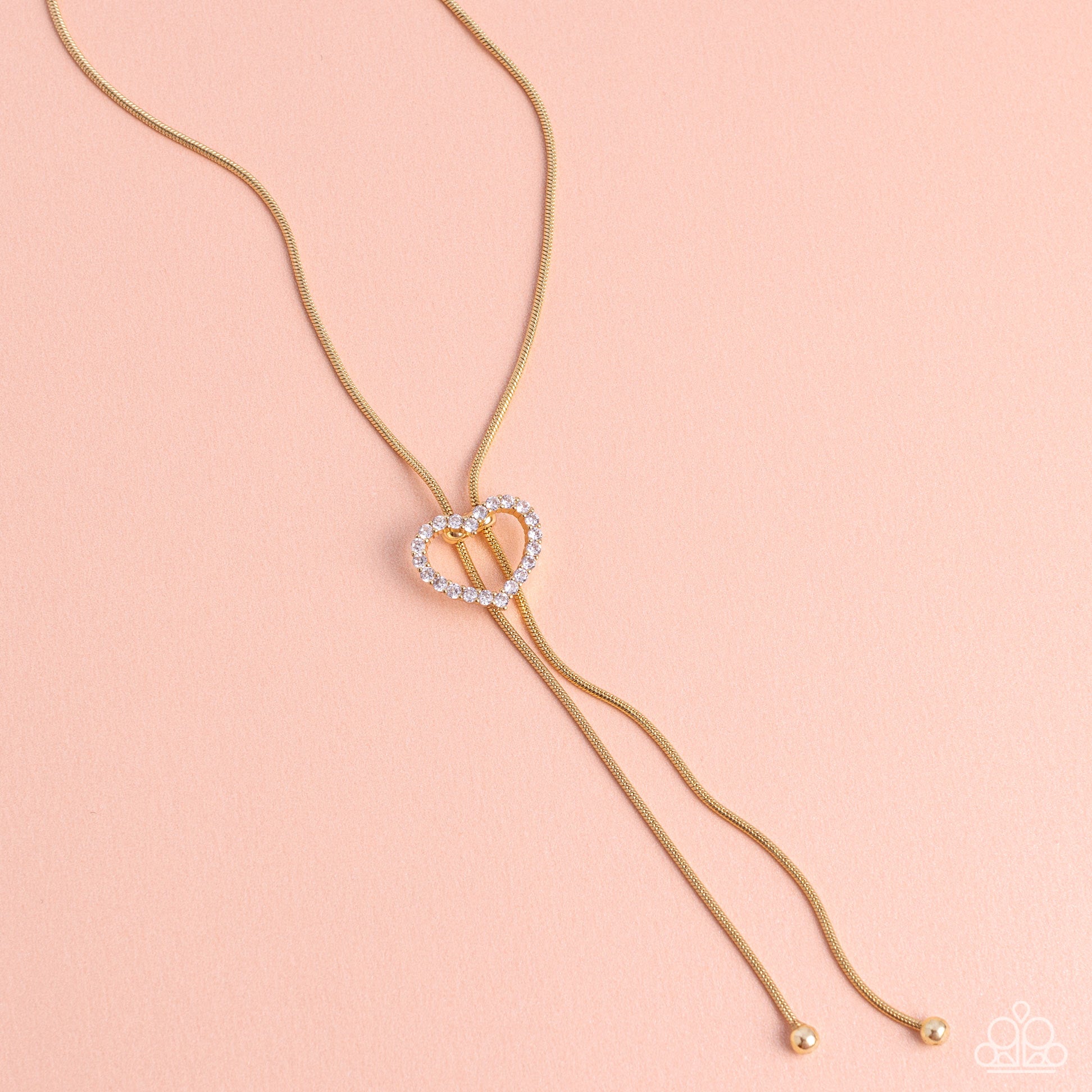 Tempting Tassel Gold Heart Bolo Necklace - Paparazzi Accessories  A dainty white rhinestone-encrusted heart silhouette slides along dainty strands of glistening gold snake chain for a timeless, refined tassel. Features a bolo closure.  Sold as one individual necklace. Includes one pair of matching earrings.  Sku:  P2DA-GDXX-327XX