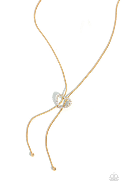 Tempting Tassel Gold Heart Bolo Necklace - Paparazzi Accessories  A dainty white rhinestone-encrusted heart silhouette slides along dainty strands of glistening gold snake chain for a timeless, refined tassel. Features a bolo closure.  Sold as one individual necklace. Includes one pair of matching earrings.  Sku:  P2DA-GDXX-327XX