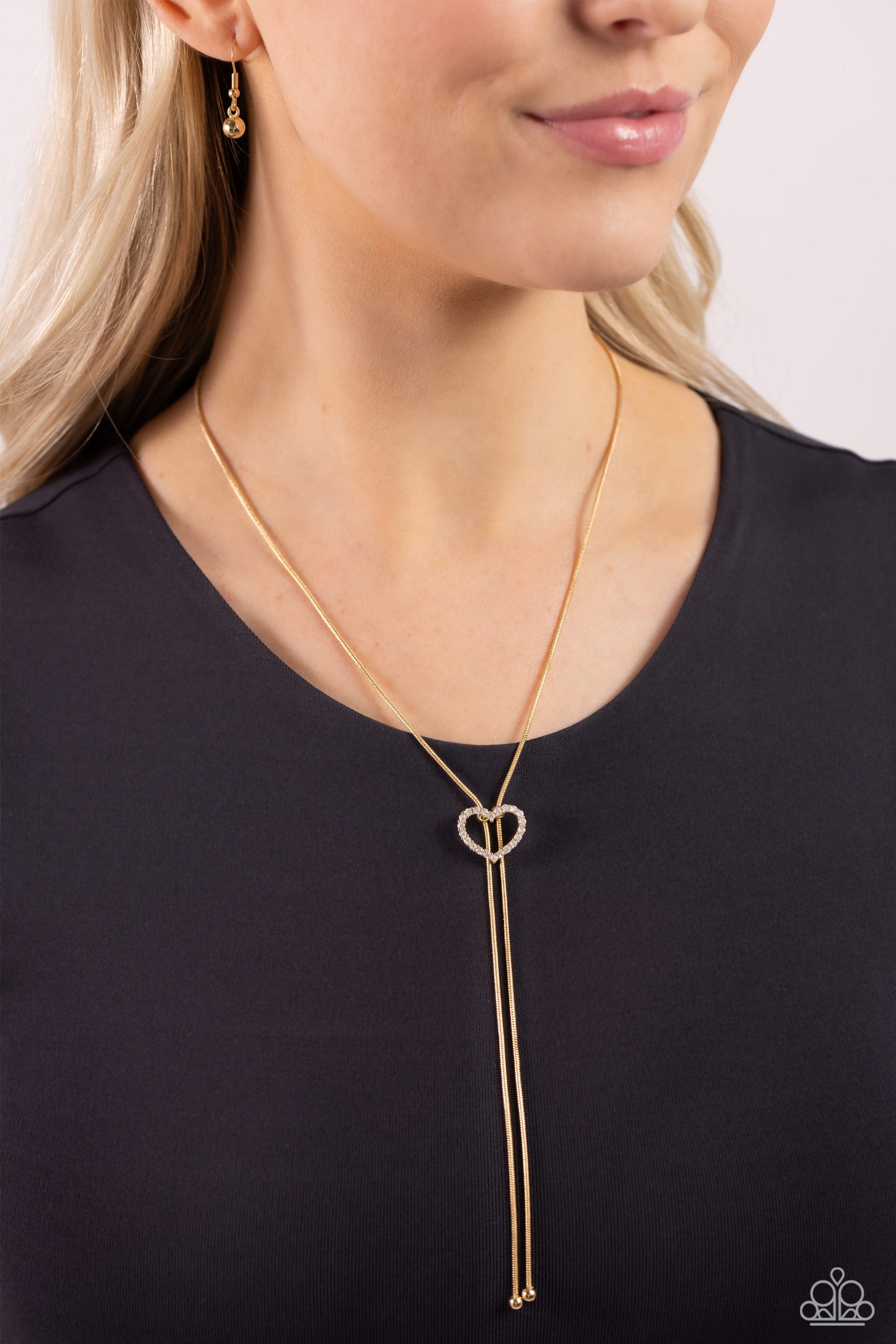 Tempting Tassel Gold Heart Bolo Necklace - Paparazzi Accessories  A dainty white rhinestone-encrusted heart silhouette slides along dainty strands of glistening gold snake chain for a timeless, refined tassel. Features a bolo closure.  Sold as one individual necklace. Includes one pair of matching earrings.  Sku:  P2DA-GDXX-327XX