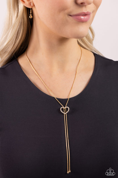Tempting Tassel Gold Heart Bolo Necklace - Paparazzi Accessories  A dainty white rhinestone-encrusted heart silhouette slides along dainty strands of glistening gold snake chain for a timeless, refined tassel. Features a bolo closure.  Sold as one individual necklace. Includes one pair of matching earrings.  Sku:  P2DA-GDXX-327XX