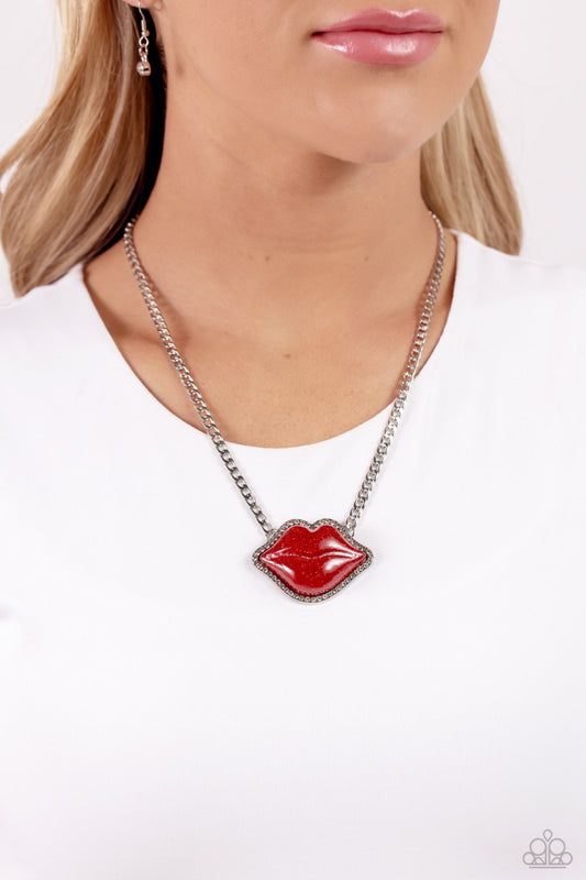 Lip Locked Red Necklace - Paparazzi Accessories  Featuring a glittery finish, an oversized red lip pendant swings from the bottom of a silver link chain below the collar for a romantic statement. White rhinestones border the charm for additional stunning detail. Features an adjustable clasp closure.  Sold as one individual necklace. Includes one pair of matching earrings.  P2ST-RDXX-124XX