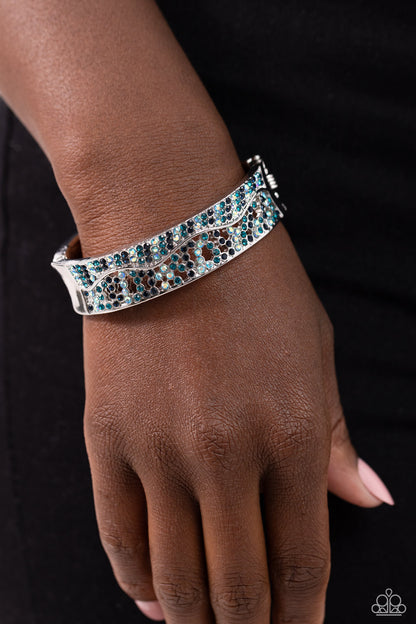 Wavy Whimsy Blue Hinge Bracelet - Paparazzi Accessories  Dusted in sections of dainty Montana, blue iridescent, and blue rhinestones, asymmetrically wavy thick silver bars boldly cross around the wrist in an airy pattern creating a gritty yet glamorous cuff.  Sold as one individual bracelet.  Sku:  P9RE-BLXX-243XX