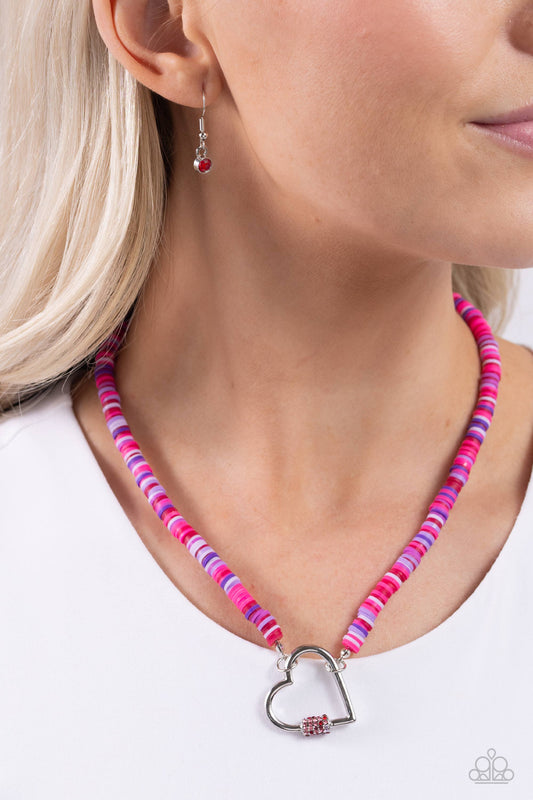 Clearly Carabiner Red Heart Necklace - Paparazzi Accessories  Infused along an invisible string, a collection of various pink, red, and purple clay discs coalesce around the collar for a vivacious display. Featuring a purple, pink, and red rhinestone-encrusted carabiner accent, a silver heart frame connects to the bottom of the multicolored strand for a romantic finish. Features an adjustable clasp closure.  Sold as one individual necklace. Includes one pair of matching earrings.  SKU: P2WH-RDXX-340XX