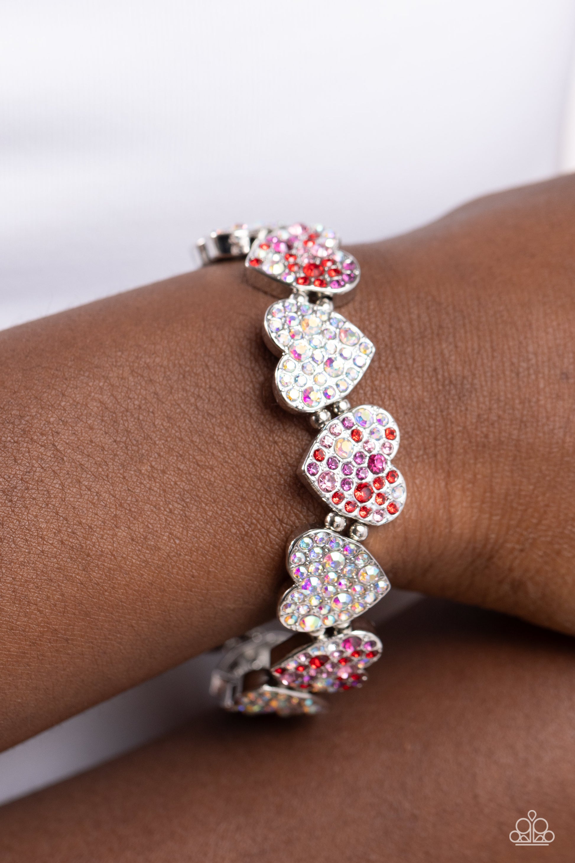 Headliner Heart Multi Rhinestone Stretch Bracelet - Paparazzi Accessories  Dotted with various sizes of dainty fuchsia, light rose, purple, red, and iridescent rhinestones, sleek silver hearts alternating in direction link together around the wrist along a stretchy band for a flirtatious finish. Due to its prismatic palette, color may vary.  Sold as one individual bracelet.  SKU: P9RE-MTXX-149XX