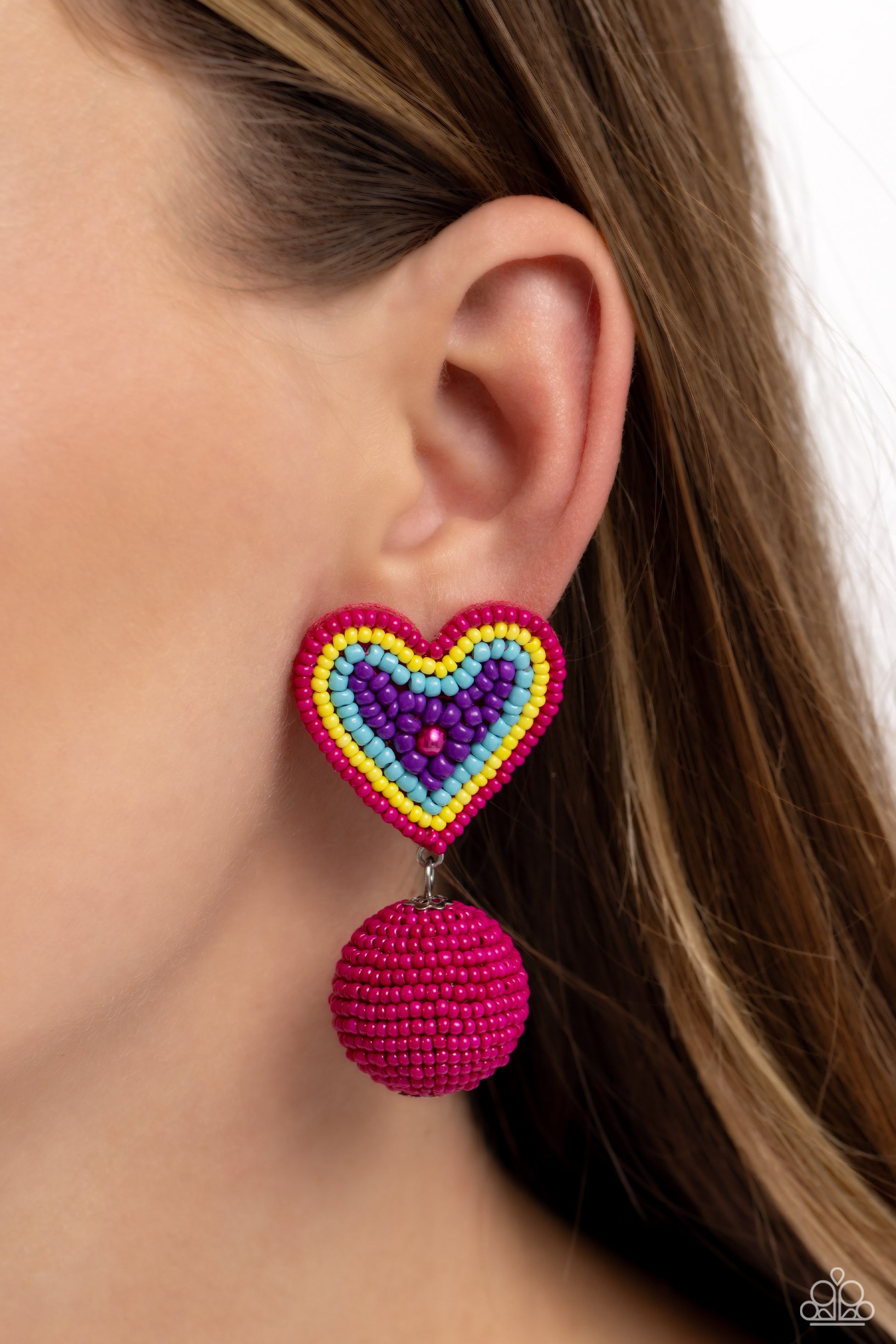 Spherical Sweethearts Multi Seed Bead Heart Post Earring - Paparazzi Accessories  Featuring a hot pink pearl center, a hot pink, yellow, turquoise, and purple seed bead heart frame gives way to strands of hot pink seed beads that decoratively spin around a spherical frame, resulting in a colorful three-dimensional display. Earring attaches to a standard post fitting.  Sold as one pair of post earrings.  P5PO-MTXX-106XX