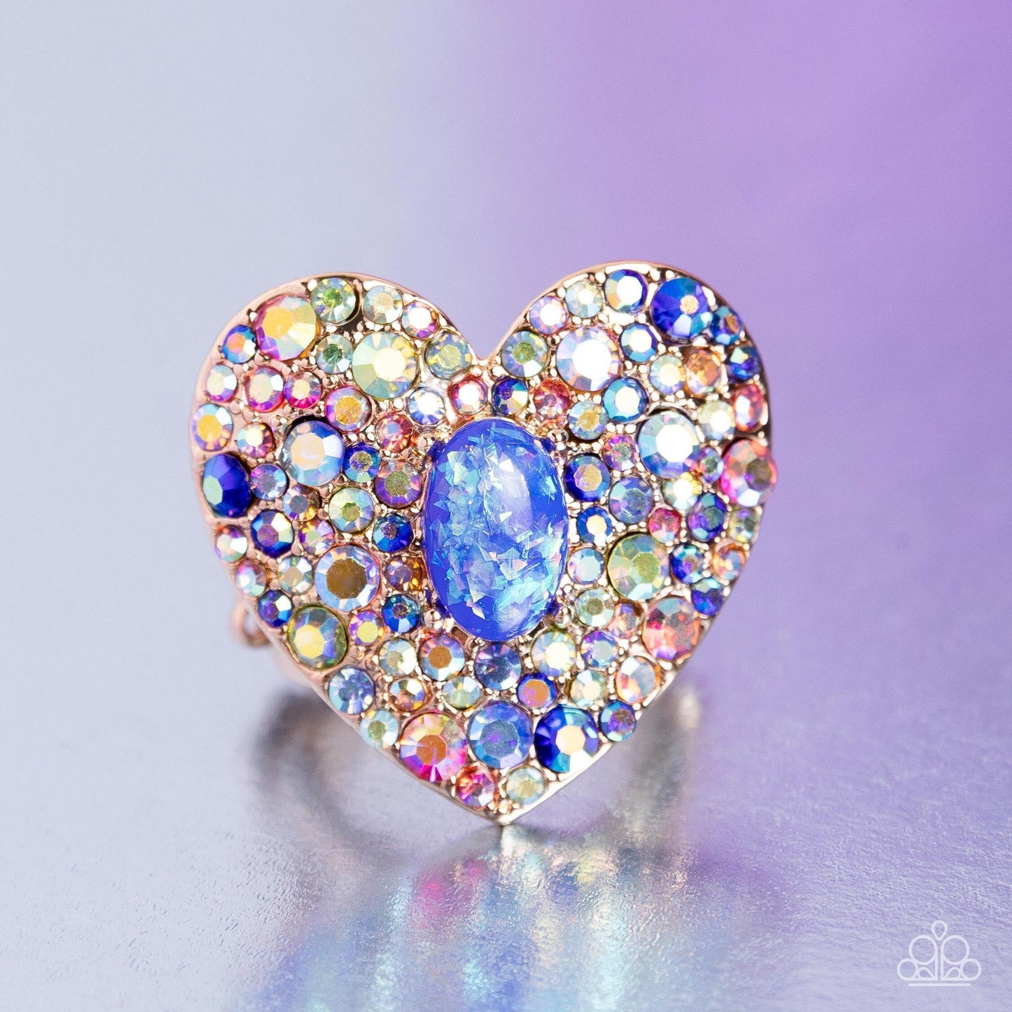 Bejeweled Beau Blue Ring - Paparazzi Accessories  Encrusted in brilliant multicolored and iridescent rhinestones, a glittery gold heart frame adorns the center of an airy gold band for a flirtatious finish. Featuring iridescent flecks, an opalescent blue oval bead is pressed in the center of the heart frame for additional eye-catching shimmer. Features a stretchy band for a flexible fit. Due to its prismatic palette, color may vary.  Sold as one individual ring.  P4ST-BLXX-029XX
