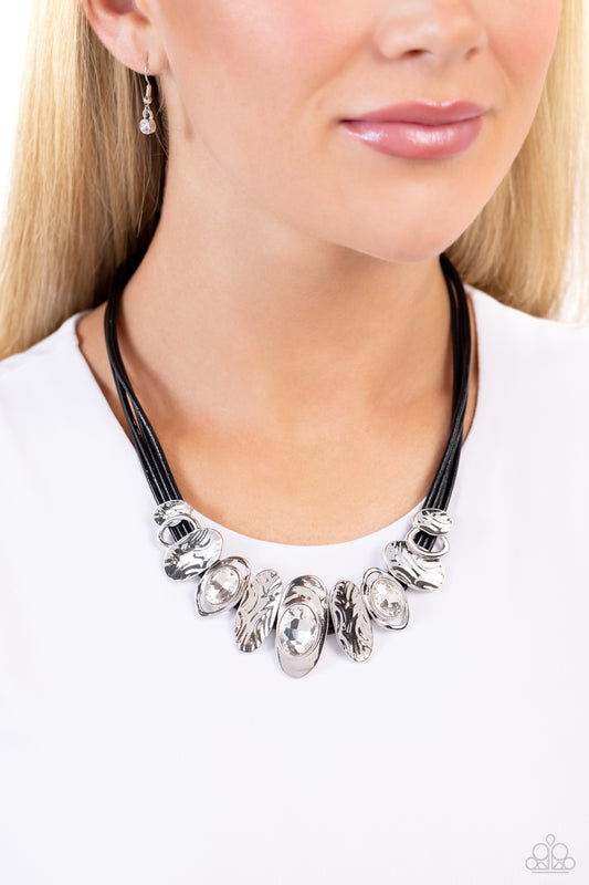 Sliding Splendor Black Necklace - Paparazzi Accessories  Featuring a lightly hammered sheen, asymmetrical silver ovals, some with airy silhouettes and exaggerated gem centers, give off a hand-made feel as they shift and slide through multiple strands of black cording for an artisanal design below the collar. Features an adjustable clasp closure.  Sold as one individual necklace. Includes one pair of matching earrings.  Sku:  P2RE-BKXX-482XX