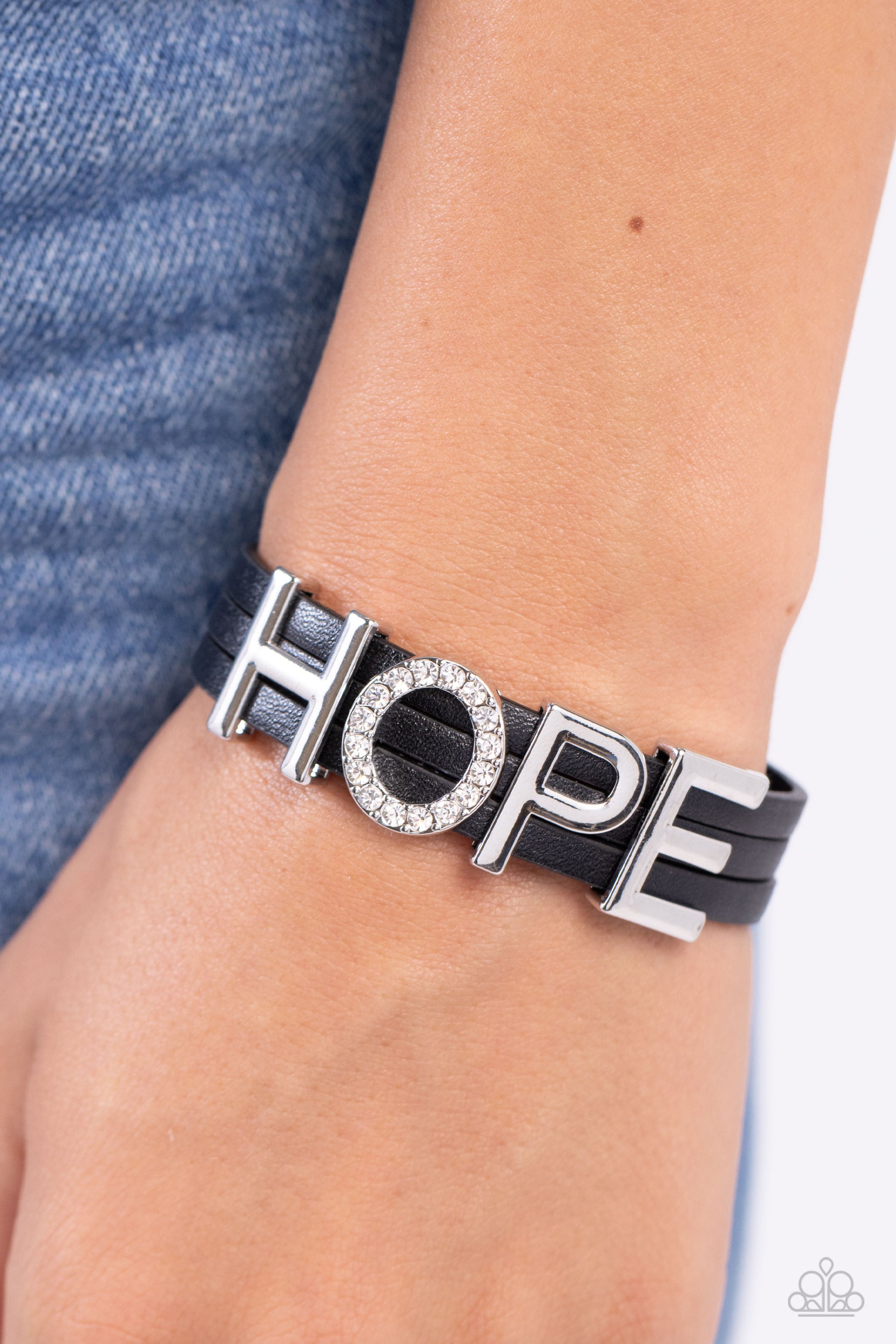 Hopeful Haute Black Wrap Bracelet - Paparazzi Accessories  Threaded along layers of black leather strands, glistening silver letters form the word "HOPE" with the "O" embossed in white rhinestones for a dazzling statement. Features a magnetic closure.  Sold as one individual bracelet.  SKU: P9SE-BKXX-345XX