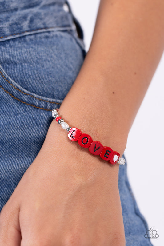 Love Language Red Stretch Bracelet - Paparazzi Accessories  Infused on an elastic stretchy band, white pearls, red seed beads, silver studs, and red beads spelling out the word "LOVE" with a white heart bead aside it wraps around the wrist for a sentimental, youthful display.  Sold as one individual bracelet.  P9WH-RDXX-194XX