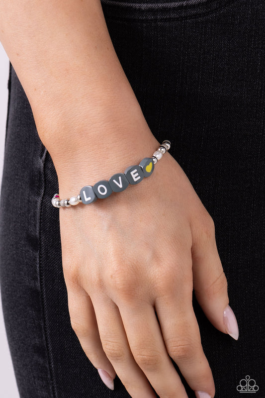 Love Language Silver Stretch Bracelet - Paparazzi Accessories  Infused on an elastic stretchy band, white pearls, gray, hot pink, and yellow seed beads, silver studs, and gray beads spelling out the word "LOVE" with a yellow heart bead aside it wraps around the wrist for a sentimental, youthful display.  Sold as one individual bracelet.  P9WH-SVXX-259XX