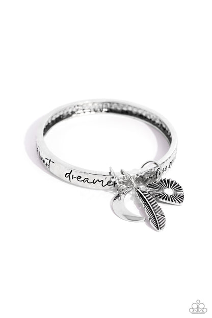 Free-Spirited Fantasy Silver Inspirational Bangle Bracelet - Paparazzi Accessories  A hammered silver bangle featuring a textured feather, sleek crescent moon, and textured heart charms wraps around the wrist for an artisan-inspired fashion. Painted in a black hue, the phrases “free spirit," "wild heart,” and "dreamer" run horizontally across the cuff for an inspirational finish.  Sold as one individual bracelet.  Sku:  P9WD-SVXX-233XX