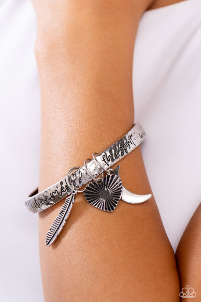 Free-Spirited Fantasy Silver Inspirational Bangle Bracelet - Paparazzi Accessories  A hammered silver bangle featuring a textured feather, sleek crescent moon, and textured heart charms wraps around the wrist for an artisan-inspired fashion. Painted in a black hue, the phrases “free spirit," "wild heart,” and "dreamer" run horizontally across the cuff for an inspirational finish.  Sold as one individual bracelet.  Sku:  P9WD-SVXX-233XX