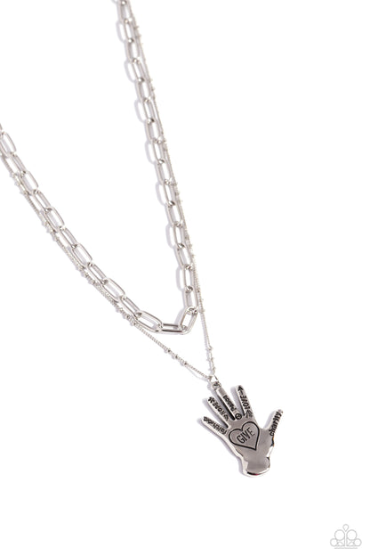 Giving a Hand Silver Inspirational Necklace - Paparazzi Accessories  Layered beside a silver paperclip chain, a silver satellite chain with a silver hand charm cascades down the chest for a seasonal statement. Stamped on each silver finger, words like "faith," "hope," "peace," "love," and "charity" stand out while the palm hosts a stamped heart with the word "give" for an inspiring finish. Features an adjustable clasp closure.